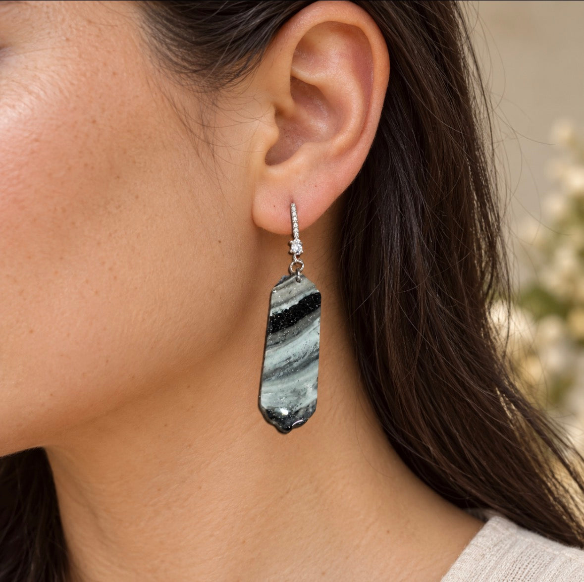 A close-up of a woman's ear wearing a silver-tone dangle earring with a polished black, white, and gray striped stone pendant.