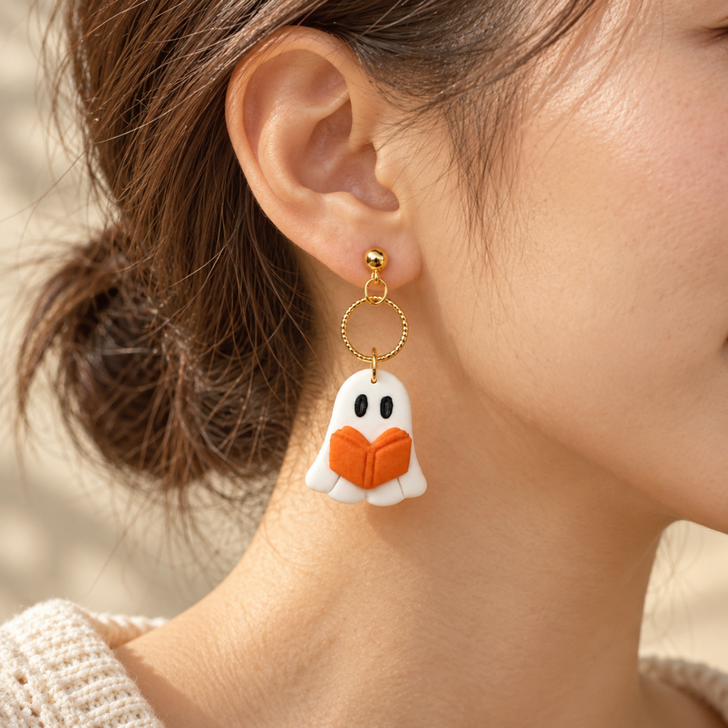 A close-up of a person wearing a dangling earring with a white ghost-like charm featuring black eyes and an orange book.